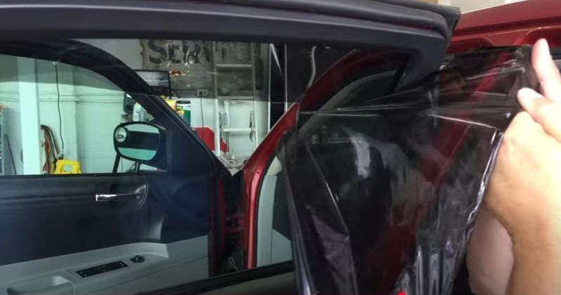 A person actively removes window tint from a car window, providing insight into how do you remove window tint from a car window.