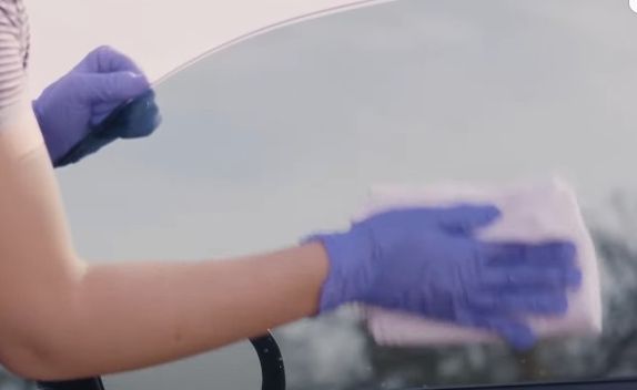 A person diligently cleans a car window with a cloth, demonstrating how to clean tinted windows for improved appearance and clarity